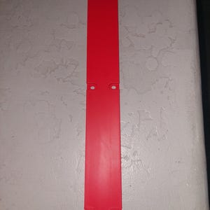 May include: A long, bright red plastic strip with four evenly spaced holes. The strip is about 12 inches long and 1 inch wide.