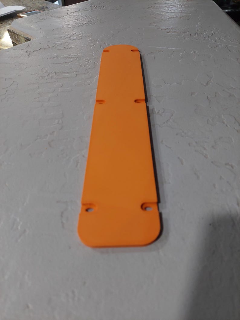 May include: Bright orange, rectangular object with rounded ends and several small holes. The object is long and narrow, with a flat surface. The color is a vibrant, solid orange.