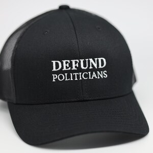 Może przedstawiać: Czarna czapka typu trucker z białym haftem "DEFUND POLITICIANS". Czapka ma siatkowy tył i zakrzywiony daszek. Codzienny dodatek do noszenia na co dzień.