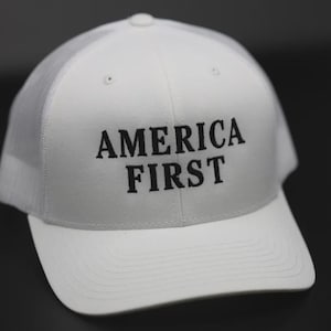 Może przedstawiać: Biała czapka trucker z czarnym haftem z napisem "AMERICA FIRST".