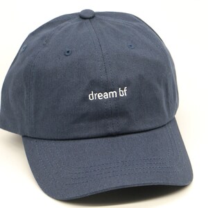 Pode incluir: Um boné de beisebol azul marinho com um logotipo branco bordado que diz "dream bf".