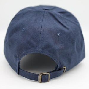 May include: A navy blue baseball cap with a curved peak, adjustable strap, and metal buckle. The cap has a classic six-panel design with a button on top and eyelets for ventilation. The back strap is adjustable.