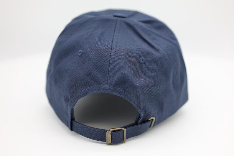 May include: A navy blue baseball cap with a curved peak, adjustable strap, and metal buckle. The cap has a classic six-panel design with a button on top and eyelets for ventilation. The back strap is adjustable.