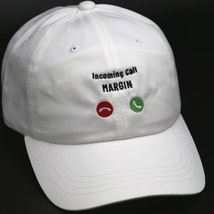 May include: White baseball cap with the text "Incoming Call MARGIN" embroidered on the front. The text is in black and there are red and green phone icons on either side of the text.