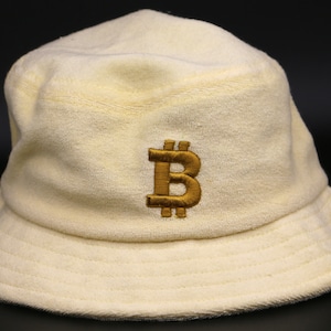 May include: A cream-colored bucket hat with a gold embroidered Bitcoin symbol.