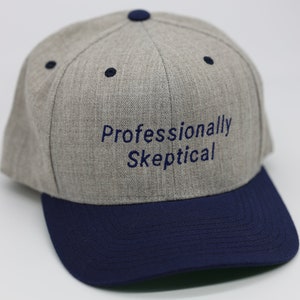 Könnte beinhalten: Eine graue und marineblaue Baseballkappe mit dem Text "Professionally Skeptical" auf der Vorderseite gestickt.