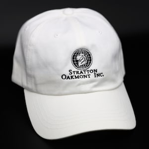 May include: White baseball cap with a black embroidered logo that says "Stratton Oakmont Inc."