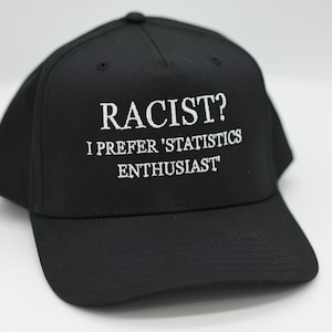 May include: Black baseball cap with the text "RACIST? I PREFER 'STATISTICS ENTHUSIAST'" embroidered in white. The cap has a curved brim and a button on top. A humorous accessory.