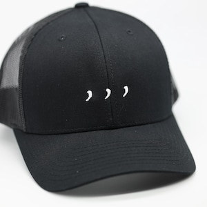 Pode incluir: Boné de caminhoneiro preto com aba curva e parte traseira em tela. A frente do boné apresenta três apóstrofos brancos bordados em linha. Um estilo clássico, adequado para uso casual.