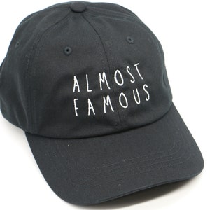 May include: A black baseball cap with white embroidery that reads "Almost Famous".