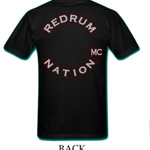 Puede incluir: Camiseta negra con las palabras "REDRUM NATION" en un diseño blanco arqueado. El texto está delineado en rojo. También son visibles las letras "MC". La palabra "BACK" está impresa en la parte inferior de la camiseta.