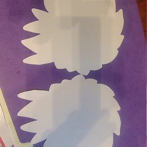 May include: Two white paper cutouts of a flower with a purple background.