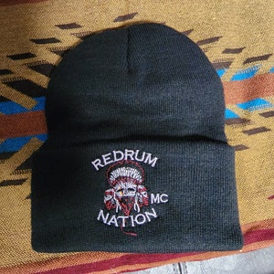 Puede incluir: Gorro negro con el texto bordado "REDRUM MC NATION". El diseño presenta una calavera con un tocado nativo americano. El gorro está hecho de un material de punto suave.