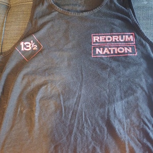 Puede incluir: Camiseta de tirantes negra con un gráfico rojo y blanco que dice "Redrum Nation" y un diamante rojo con el número "13 1/2" dentro.