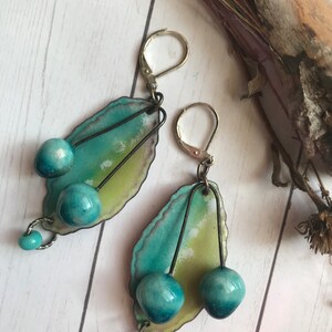 May include: Teal and green enamel earrings with silver hooks and blue glass beads. The earrings feature a leaf-shaped design with three blue glass beads on each earring.