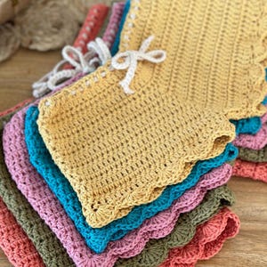 Puede incluir: Una pila de pantalones cortos de ganchillo en varios colores, incluyendo coral, verde, rosa, azul y amarillo. Los pantalones cortos tienen un borde festoneado y están hechos con un patrón de punto simple. #crochet