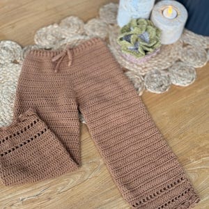 May include: Brown crocheted trousers with a drawstring waist and lace trim. The trousers are made with a soft, textured yarn.