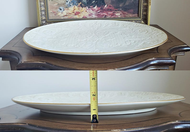 May include: A white oval serving platter with a gold rim and an embossed floral design. The platter is sitting on a wooden table.