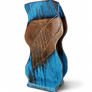 May include: A ceramic vase with a unique, abstract design. The vase features a combination of brown and blue colors. The top and sides are a vibrant blue, while the center has a textured brown pattern. The vase has a rectangular base and a curved, organic shape.