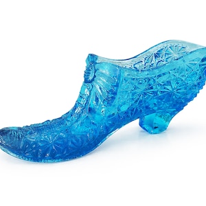 May include: A clear, blue glass slipper with detailed star and floral patterns. The shoe features a high heel and a curved design. This decorative glass slipper is reminiscent of a fairytale.