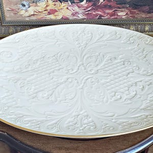 May include: A large, white, oval serving platter with a gold rim and an embossed floral design.