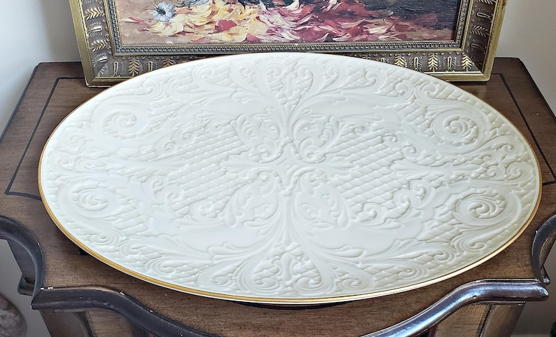 May include: A large, white, oval serving platter with a gold rim and an embossed floral design.