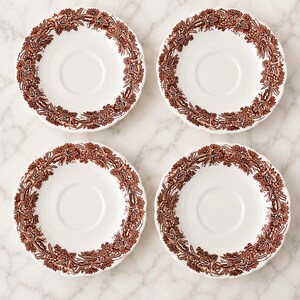 May include: A set of four round white ceramic saucers, each featuring a detailed brown transferware pattern along the rim. The design consists of intricate grapevines, leaves, and clusters of grapes encircling the center of each saucer.
