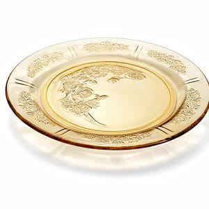 May include: A clear, amber-colored glass plate with a floral rose design. The plate features an embossed rose pattern on the inner rim and a decorative border. The plate is round and has a slightly raised edge.