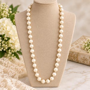 May include: A long necklace featuring a single strand of alternating large cream-colored spherical beads and small metallic silver-toned spacer beads, displayed on a neutral-toned fabric-covered bust form.