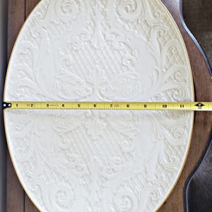 May include: A white oval serving platter with a gold rim and an embossed floral design. The platter is 12 inches in diameter.
