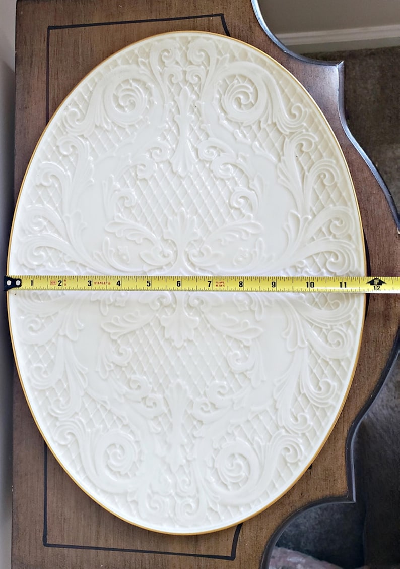 May include: A white oval serving platter with a gold rim and an embossed floral design. The platter is 12 inches in diameter.
