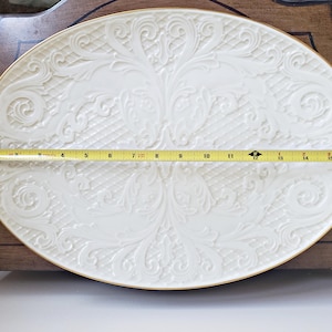 May include: A white oval serving platter with a gold rim and an embossed floral design. The platter measures 15 inches in length.