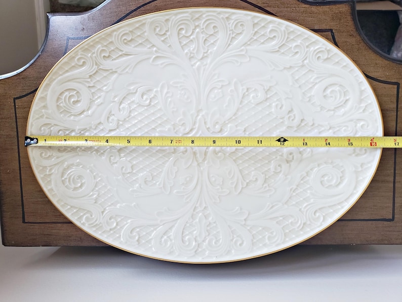 May include: A white oval serving platter with a gold rim and an embossed floral design. The platter measures 15 inches in length.