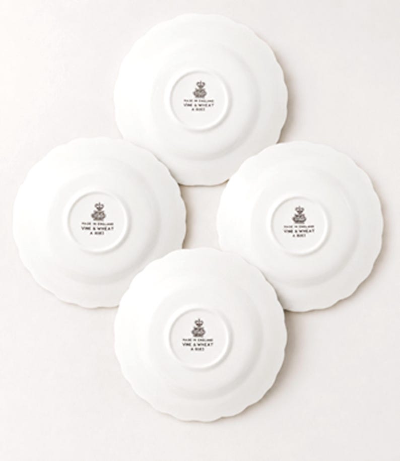 May include: Four white ceramic plates with scalloped edges, shown from the underside. Each plate features a central black stamp with a crown icon and the text MADE IN ENGLAND VINE & WHEAT A 8021, indicating the origin and collection details.
