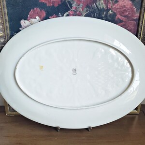 May include: White oval serving platter with a raised, textured design. The platter has a small mark on the bottom and a stamp that reads "Made in Germany".