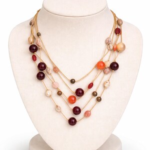 May include: A multi-strand necklace with various sized beads in shades of red, orange, pink, and beige. The beads are strung on delicate gold chains and displayed on a white jewelry bust.