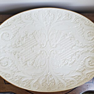 May include: A white oval serving platter with a gold rim and an embossed floral design.