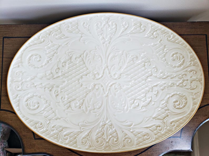 May include: A white oval serving platter with a gold rim and an embossed floral design.
