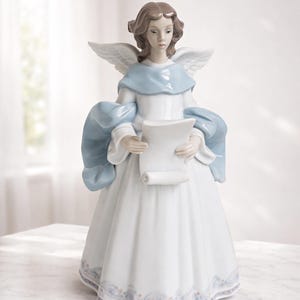May include: A porcelain angel figurine in a flowing white gown with a light blue shawl and wings. The angel holds a scroll and has brown hair. The base of the gown has a delicate floral pattern. A decorative piece for the home.
