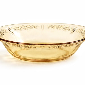 May include: A clear, amber-coloured glass bowl with a floral design around the rim. The bowl has a wide, shallow shape, suitable for serving food. The glass has a slight golden hue, and the floral pattern adds a decorative touch.