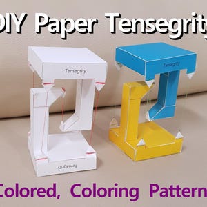 Pode incluir: Duas estruturas de tensegridade de papel, uma branca e outra com painéis azuis e amarelos. As estruturas são feitas de papel e corda e são etiquetadas como "Tensegrity".