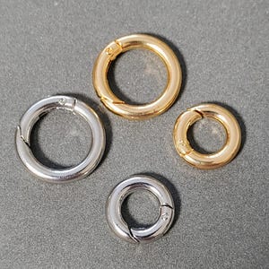 May include: Four metal key rings in two sizes. Two are silver and two are gold. The rings are open and have a spring-loaded clasp.