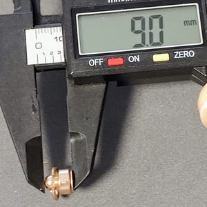 May include: A close-up of a digital caliper measuring a small gold-colored object. The caliper reads 9.0 mm.