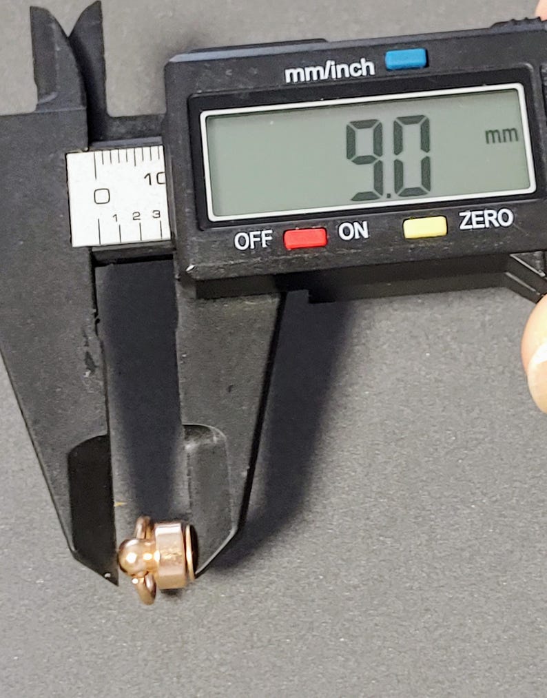 May include: A close-up of a digital caliper measuring a small gold-colored object. The caliper reads 9.0 mm.