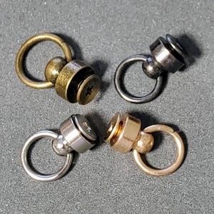 May include: Four metal swivel snap hooks with different finishes: gold, silver, brass, and black. Each hook has a small ring and a screw-on cap.