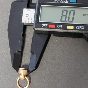 May include: A gold-toned metal ring with a small ball on top, measured at 8.0 mm using a digital caliper.