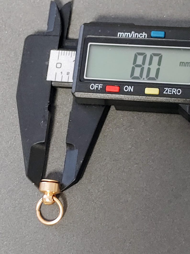 May include: A gold-toned metal ring with a small ball on top, measured at 8.0 mm using a digital caliper.