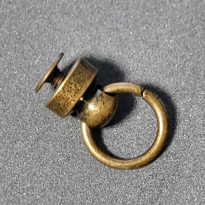 May include: A gold-toned metal swivel snap hook with a screw-on base. The hook is attached to a round metal ring.