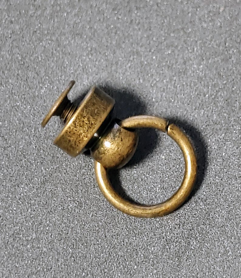 May include: A gold-toned metal swivel snap hook with a screw-on base. The hook is attached to a round metal ring.