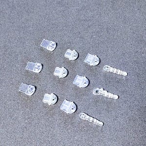 May include: A collection of clear plastic charms in various shapes, including a few that resemble small keys. The charms are scattered on a gray surface.